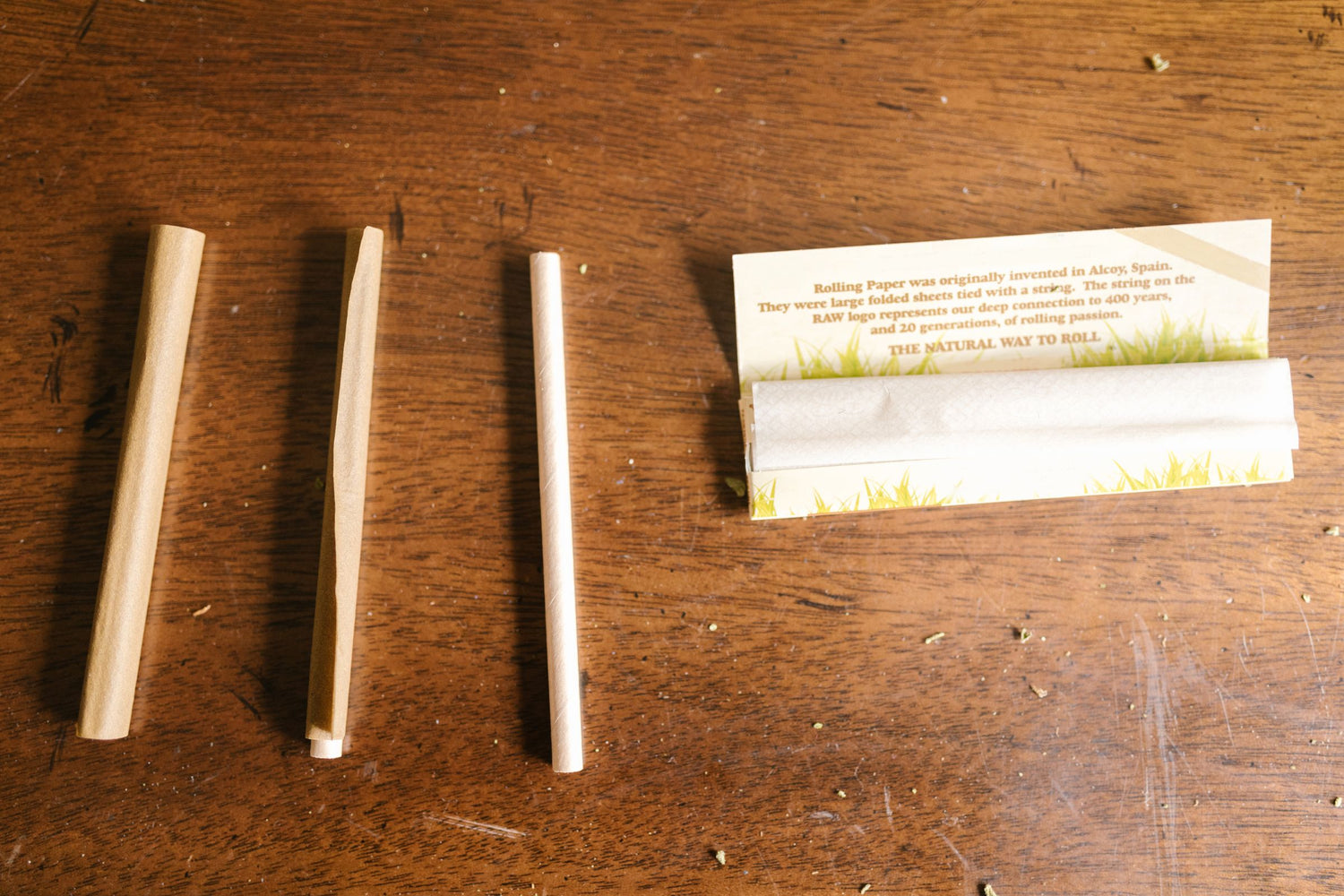 Pre-rolled cones and a pack of RAW rolling papers laid out on a wooden table